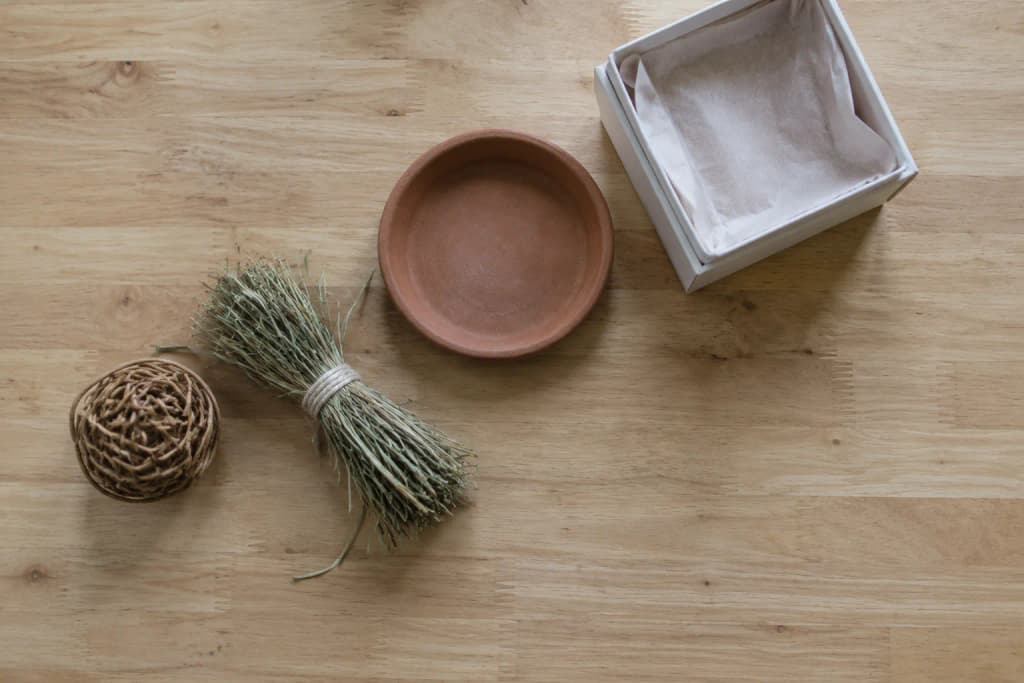 Overhead view of a willow ball, a tied bundle of hay, a terracotta dish and an empty gift box on a maple table