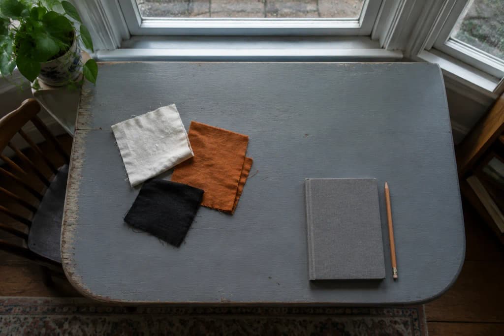 Overhead view of white, orange and black cotton scraps beside a closed notebook and pencil on a grey-blue table